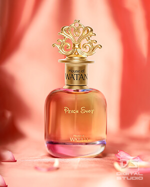 Actual premium fragrance bottle photographed in a creative studio setup with a soft peach fabric background and flower petals.
